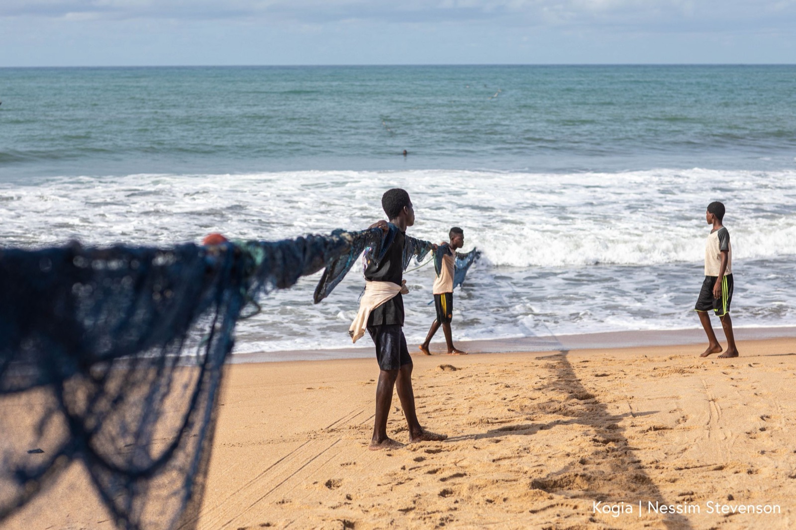 Young men hauling a fishing net from the surf on a warm coastline